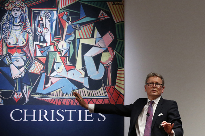 Christie's auctioneer and Global President Jussi Pylkkanen gestures during bidding for Pablo Picassos Women of Algiers (Version O), (1955), shown behind him in a poster, which sold for $179.4 million, making it the most expensive artwork sold at auction, during a sale of 20th century art at Christie's Rockefeller Center in New York, Monday, May 11, 2015.  Experts say the once unthinkable prices are driven by artworks investment value and by wealthy new and established collectors seeking out the very best works. (AP Photo/Kathy Willens)