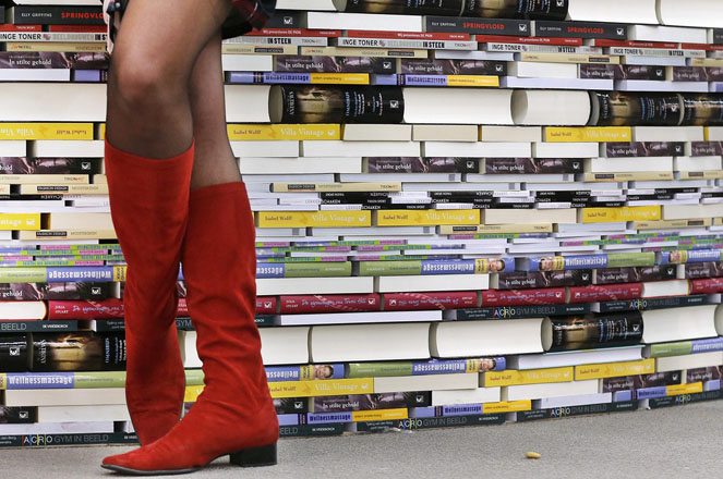 A woman with red boots stands next to books on the second day of the Book Fair that will be opened later the day in Frankfurt, Germany, Thursday, Oct. 11, 2012. New Zealand is this year's guest of honor. (AP Photo/Michael Probst)