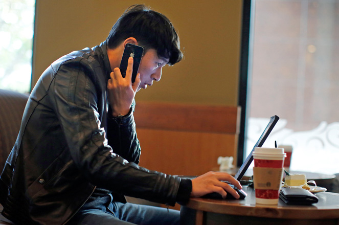 A man talks on the phone as he surfs the internet on his laptop at a local coffee shop in downtown Shanghai November 28, 2013. China's campaign against online rumours, which critics say is crushing free speech, has been highly successful in 