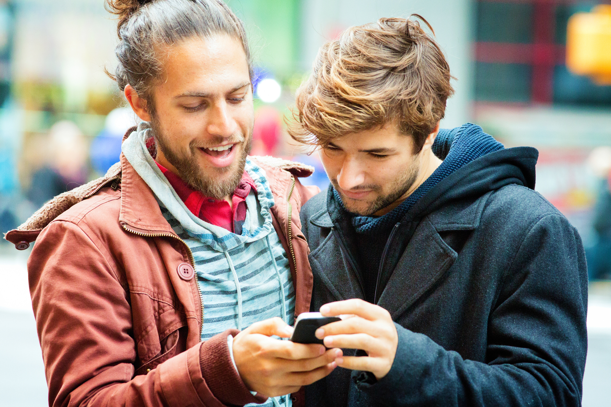 Young man sharing media with friend on mobile phone. Close-up version; they are both smiling.