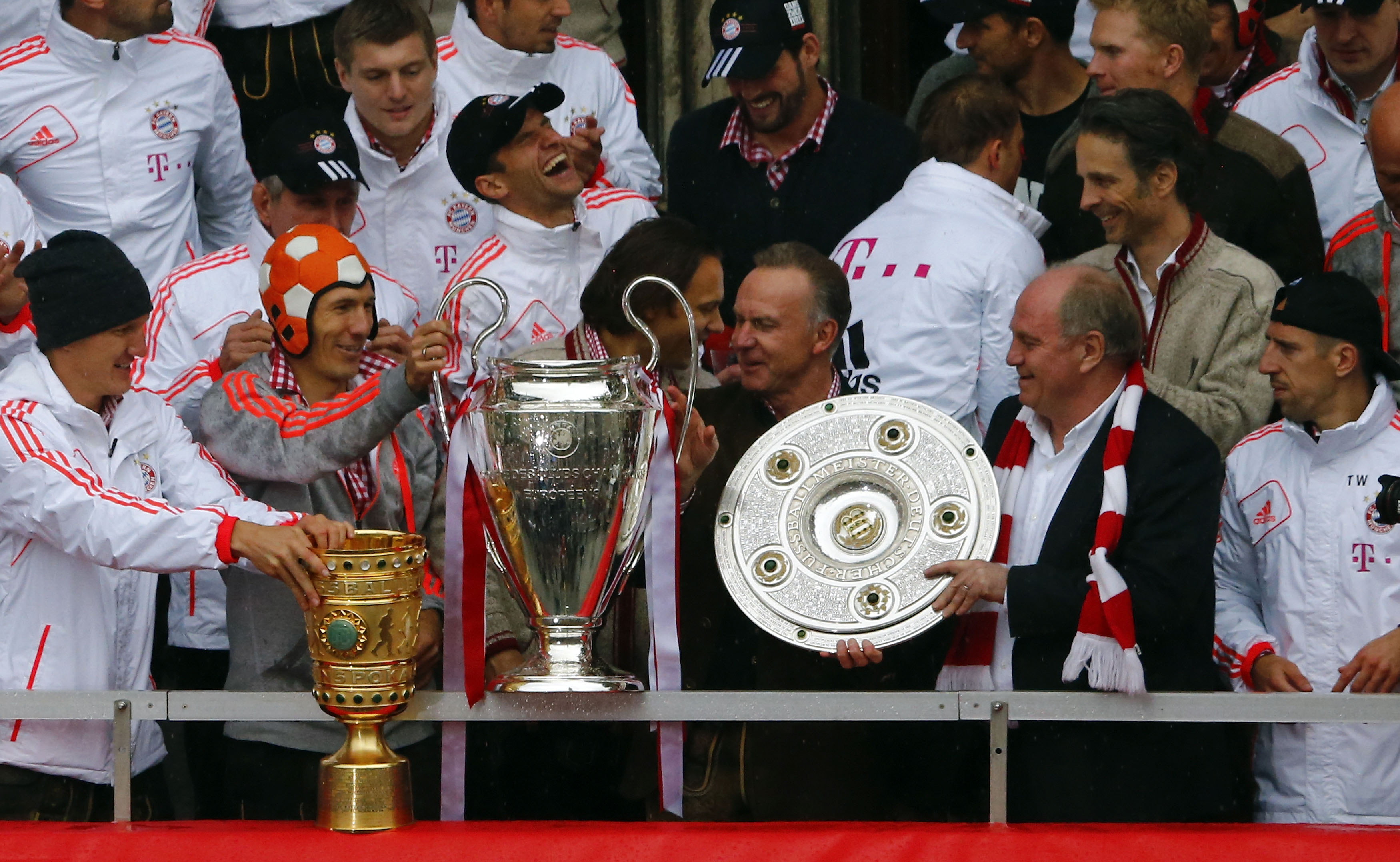 Bayern Munich's players and Chief Executive Karl-Heinz Rummenigge (3R) and President Uli Hoeness (2R) hold up German soccer cup (DFB Pokal), Champions League and German soccer championship Bundesliga trophies as they stand on the balcony of the town hall in Munich June 2, 2013. Bayern Munich completed the treble by beating VfB Stuttgart 3-2 in the German Cup final on June 1, 2013, adding the trophy to the Champions League and Bundesliga titles they have already won this season. REUTERS/Michael Dalder (GERMANY - Tags: SPORT SOCCER) - RTX1099B