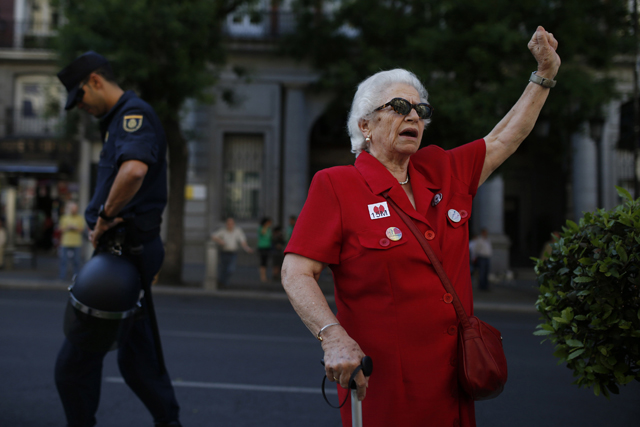 Woman wearing a 15M sticker walks past a police officer as she arrives at Puerta del Sol on third anniversary of 15M movement in central Madrid