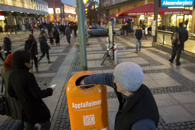 Homeless man searches waste bin for empty bottles at Alexanderplatz square in Berlin