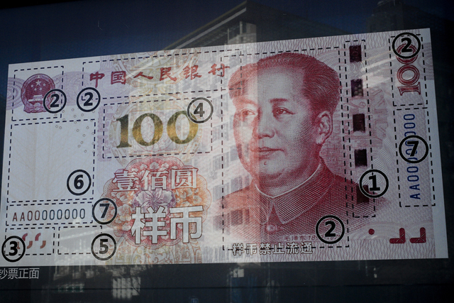 An office building is reflected on a new 100 Yuan note on display outside a bank in Beijing, Monday, Jan. 11, 2016. Barely a week into 2016, Chinese President Xi Jinping is already having a rough time of it, with a plummeting stock market, falling currency, new provocations from boisterous ally North Korea and strong prospects for a victory by the pro-independence opposition in Taiwan, which China sees as a renegade province. (AP Photo/Andy Wong)