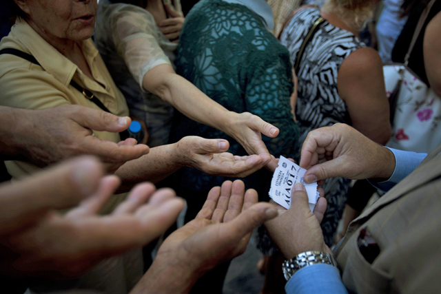 A bank employee distributes queue tags to elderly people waiting to enter a bank where they can pick up a per-person maximum of 120 euros ($134) for the week in central Athens, in this photo dated Monday, July 13, 2015. The latest incarnation of Greeces economic crisis over the span of a month saw Greece in the end accept harsh austerity measures from creditors to save the country from bankruptcy and possibly ignominiously getting kicked out of the eurozone. (AP Photo/Emilio Morenatti)