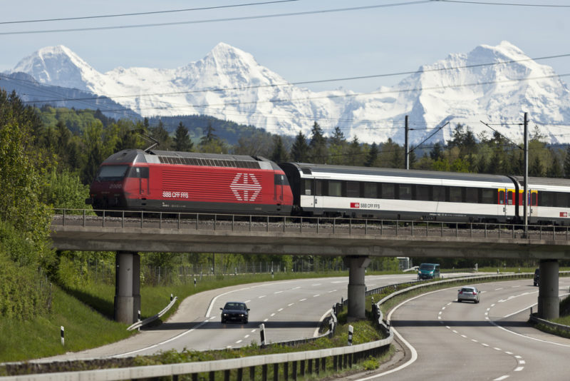 Niemand will die Kostenwahrheit im Verkehr: Bahn und Autobahn vor Schweizer Bergkulisse. Foto: Gaetan Bally (Keystone)