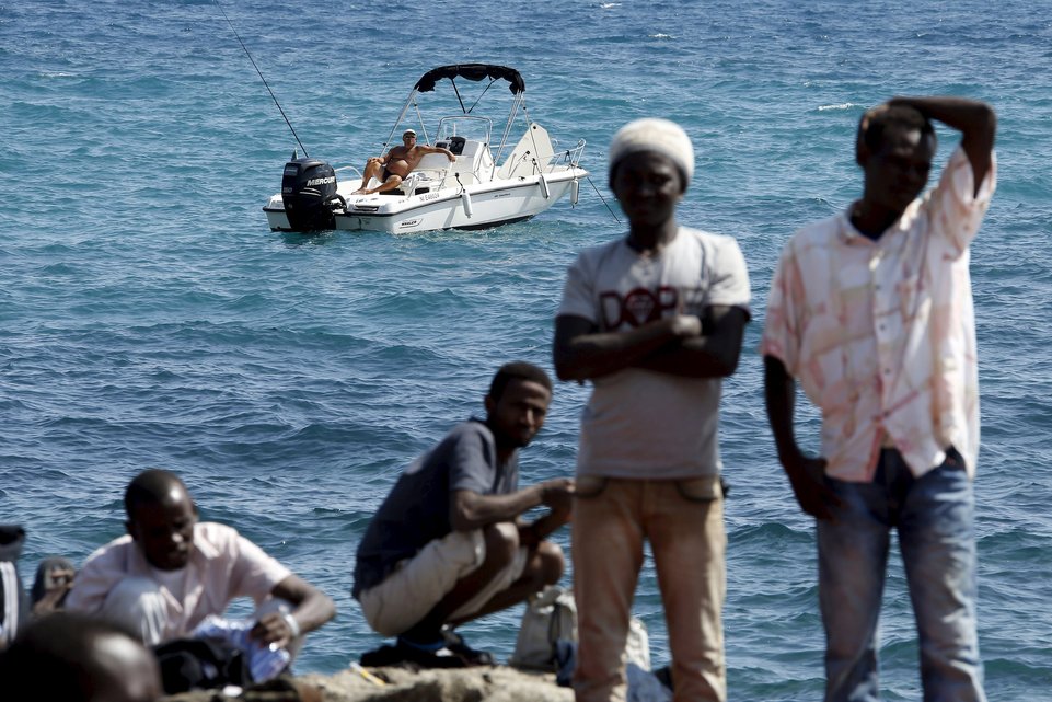 A man fishes from his boat as a group of migrants gather on the seawall at the Saint Ludovic border crossing on the Mediterranean Sea between Vintimille, Italy and Menton, France, in this June 14, 2015 file photo. Italy stepped up calls for a change to European asylum rules on Sunday as neighbouring states tightened border controls, turning back African migrants and leaving hundreds stranded at the frontier in northern Italy.  REUTERS/Eric Gaillard/Files ATTENTION EDITORS - THIS PICTURE IS PART OF THE PACKAGE "IN PLAIN SIGHT". TO FIND ALL 9 IMAGES SEARCH 'MIGRANT EUROPEAN'.      TPX IMAGES OF THE DAY
