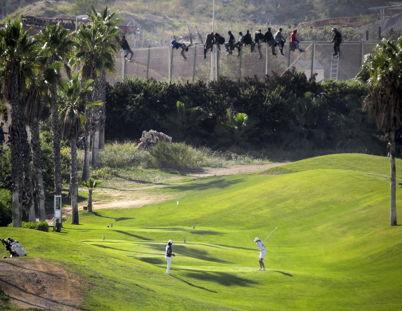 A golfer hits a tee shot as African migrants sit atop a border fence during an attempt to cross into Spanish territories between Morocco and Spain's north African enclave of Melilla, in this October 22, 2014 file photo. Italy stepped up calls for a change to European asylum rules on Sunday as neighbouring states tightened border controls, turning back African migrants and leaving hundreds stranded at the frontier in northern Italy.  REUTERS/Jose Palazon/Files ATTENTION EDITORS - THIS PICTURE IS PART OF THE PACKAGE "IN PLAIN SIGHT". TO FIND ALL 9 IMAGES SEARCH 'MIGRANT EUROPEAN'.