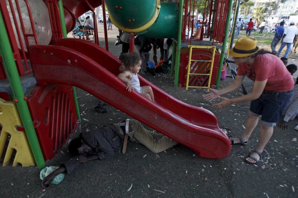 A Sudanese migrant sleeps under a slide as an Israeli girl slides down it at Levinsky park in South Tel Avi, in this June 16, 2012 file photo. Italy stepped up calls for a change to European asylum rules on Sunday as neighbouring states tightened border controls, turning back African migrants and leaving hundreds stranded at the frontier in northern Italy.  REUTERS/Baz Ratner/Files ATTENTION EDITORS - THIS PICTURE IS PART OF THE PACKAGE "IN PLAIN SIGHT". TO FIND ALL 9 IMAGES SEARCH 'MIGRANT EUROPEAN'.