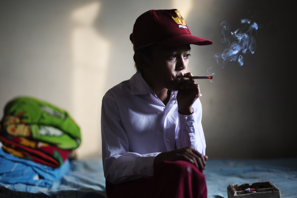 Ilham Hadi, who has smoked up to two packs a day, poses for a photo wearing his third grade uniform while smoking in his bedroom on February 14, 2014. (Photo By: Michelle Siu)