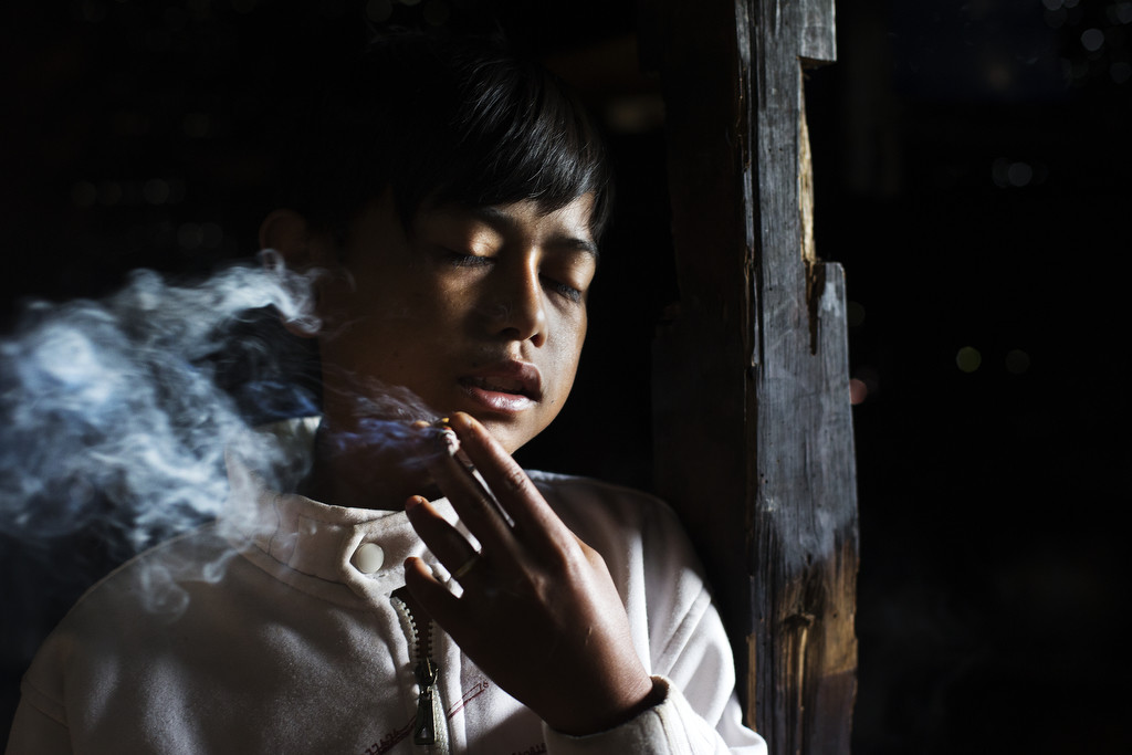 Illham Muhamad, who has smoked since he was five years old, poses for a photo as he slowly inhales his first cigarette of the day at his grandmother's home on February 10, 2014. He does not attend school and if his grandmother refuses to give him money to buy cigarettes he will go through withdrawal and cry and throw fits. (Photo By: Michelle Siu)