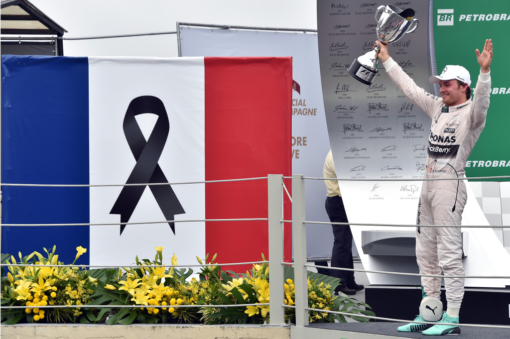 Mercedes' Formula One German driver Nico Rosberg celebrates after winning the Brazilian Grand Prix, beside a French flag with a black ribbon to remember those people killed during the Paris November 13 attacks, at the Interlagos racetrack in Sao Paulo, on November 15, 2015. AFP PHOTO / NELSON ALMEIDA