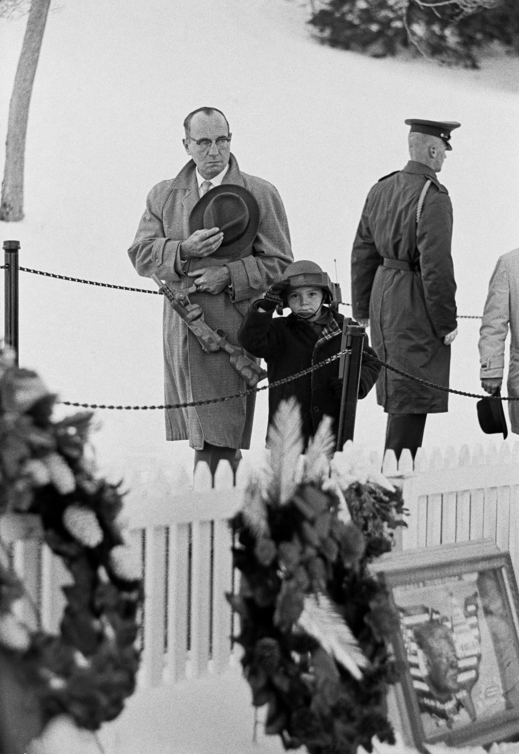 USA. Washington, D.C. 1963. A father and boy with a toy helmet and gun give a salute at the grave of John F. Kennedy in Arlington cemetary.