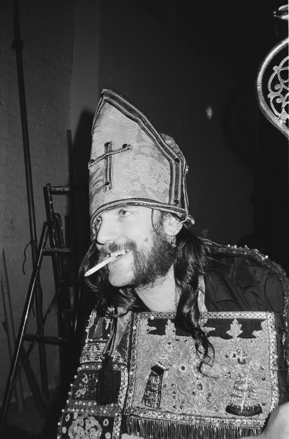 LONDON - 1st JULY: Lemmy Kilmister from Motorhead posed wearing a bishop's mitre hat and smoking a cigarette during the photo session for the 'Killed By Death' single in Pimlico, london in July 1984. (Photo by Fin Costello/Redferns)
