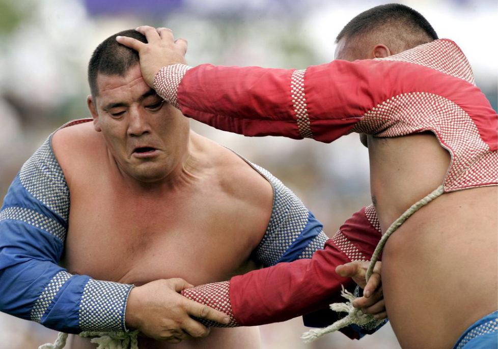 epa01063708 Mongolian wrestlers in traditional attire grapple during wrestling competitions as referees look on during the Naadam festival at the National Stadium in Ulaanbaatar, Mongolia, 11 July 2007. Mongolia is celebrating the Naadam festival from the 11-13 July 2007, the most important festival of the year, with horseracing, wrestling and archery - known as the three 'manly sports'. EPA/MICHAEL REYNOLDS