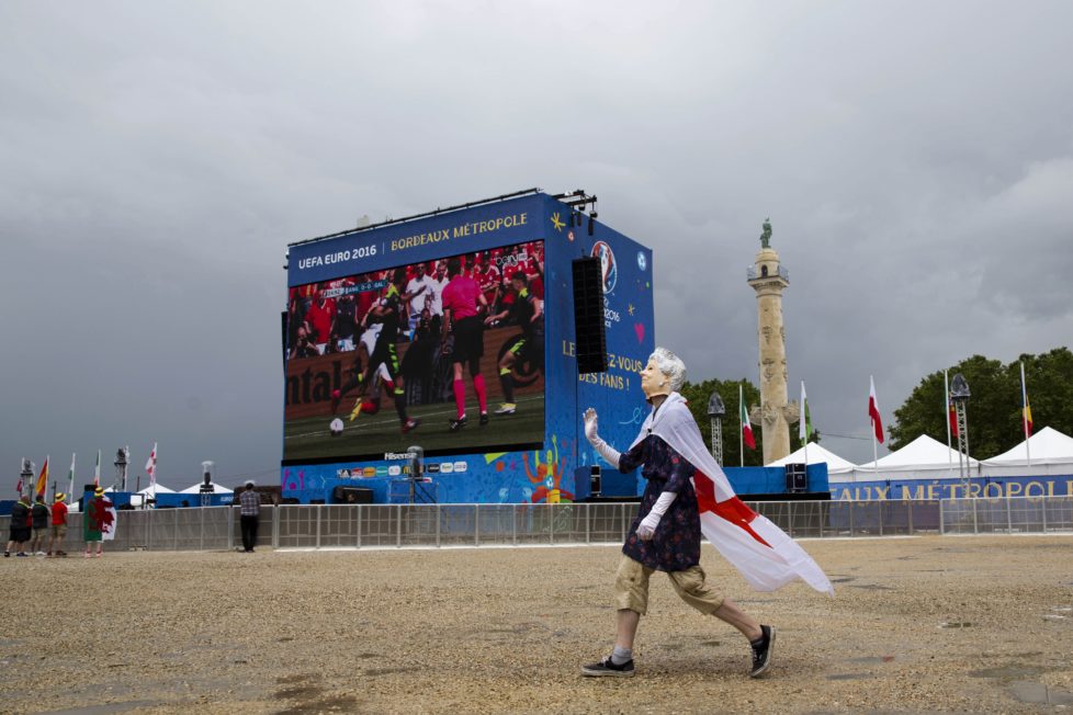 A British fan wearing a mask representing Britain's Queen Elizabeth II waves to other fans as they watch the Euro 2016 Group B soccer match between England and Wales in Bordeaux's fan zone, France, Thursday, June 16, 2016. (AP Photo/Hassan Ammar)