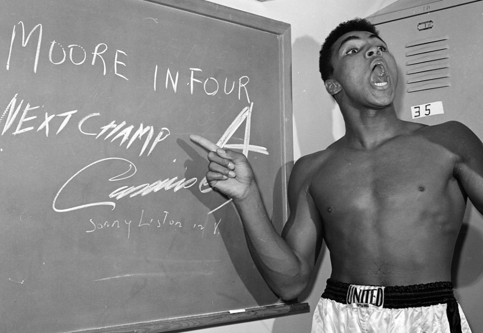FILE - In this Nov. 15, 1962, file photo, young heavyweight boxer Cassius Clay, who later changed his name to Muhammad Ali, points to a sign he wrote on a chalk board in his dressing room before his fight against Archie Moore in Los Angeles, predicting he'd knock Moore out in the fourth round, which he went on to do. The sign also predicts Clay will be the next champ via a knockout over Sonny Liston in eight rounds. He did it in seven rounds. Ali turns 70 on Jan. 17, 2012. (AP Photo/Harold P. Matosian, File)