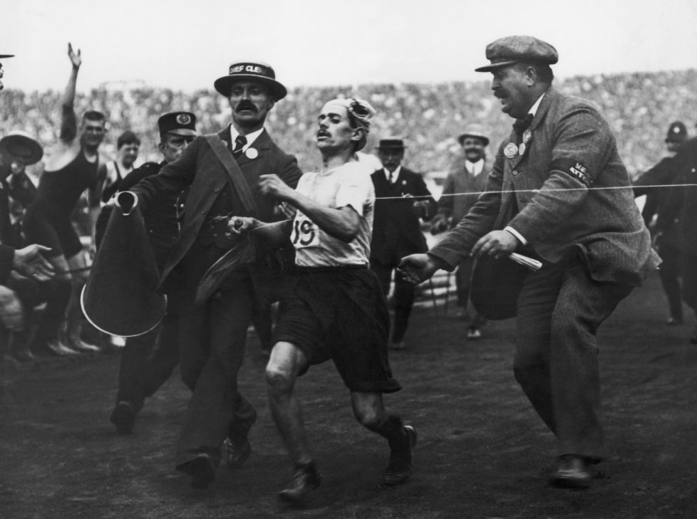 Dorando Pietri of Italy, on the verge of collapse, is helped across the finish line in the Marathon event of the Olympic Games in London, 24th July 1908. He was subsequently disqualified and the title was given to John Hayes of the USA. (Photo by Hulton Archive/Getty Images)