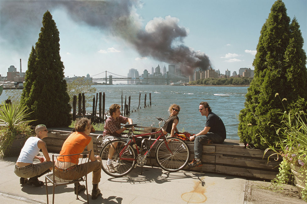 USA. Brooklyn, New York. September 11, 2001. Young people relax during their lunch break along the East River while a huge plume of smoke rises from Lower Manhattan after the attack on the World Trade Center. (KEYSTONE/MAGNUM PHOTOS/Thomas Hoepker)