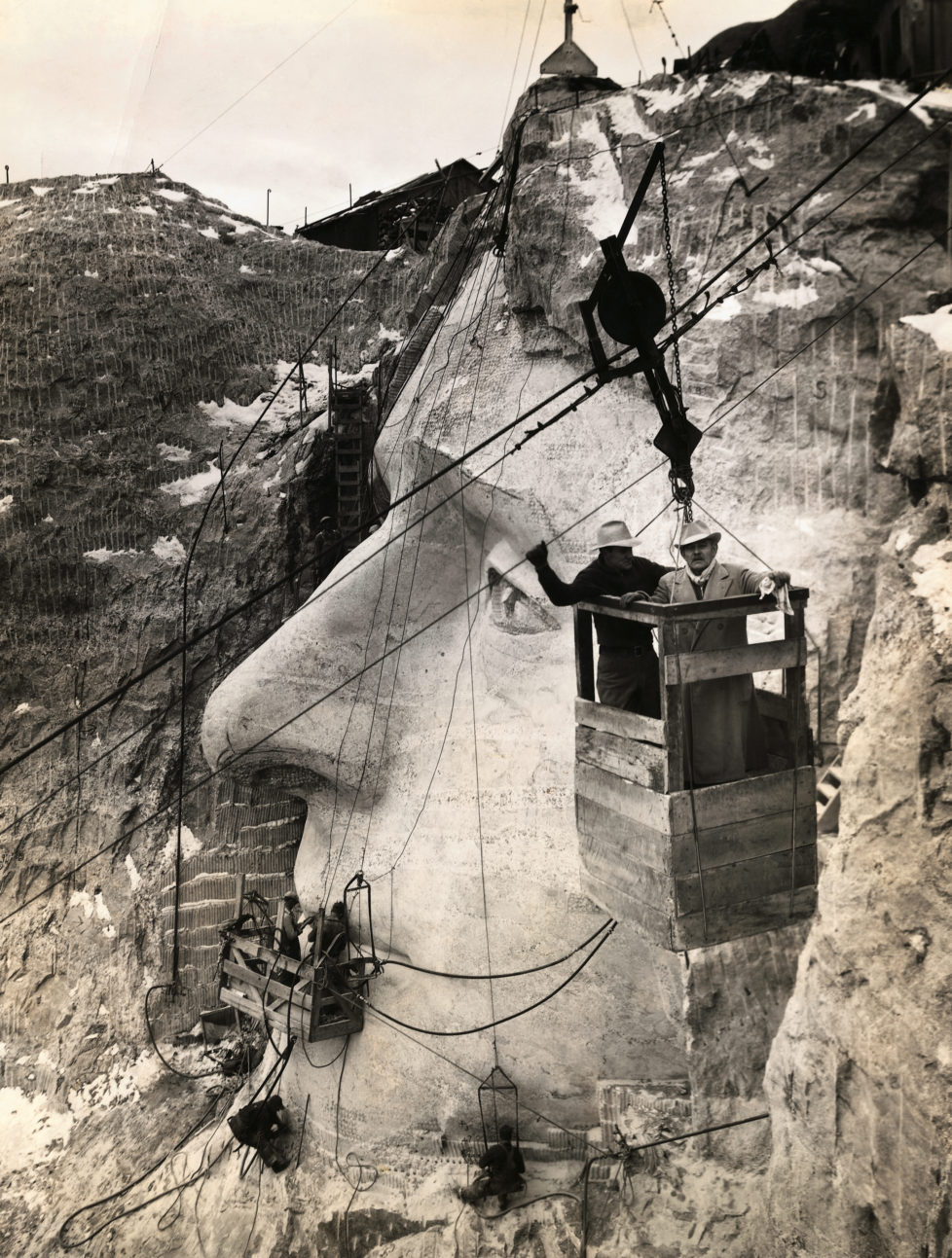 American sculptor Gutzon Borglum, who is leading the Mount Rushmore National Memorial project, and his son, Lincoln, inspect the Jefferson head from an aerial tram. (Photo by George Rinhart/Corbis via Getty Images)
