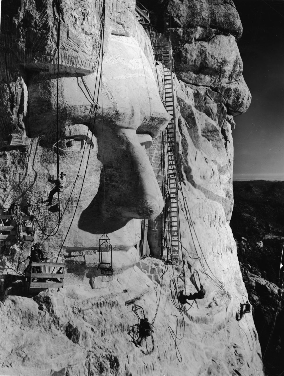 American sculptor Gutzon Borglum (1867 - 1941) (hanging below the eye) and several of his crew work on carving the head of American President Abraham Lincoln, part of the Mount Rushmore National Memorial, Keystone, South Dakota, 1930s. Lincoln's head, the third head carved, was completed and dedicated on September 17, 1937. (Photo by Frederic Lewis/Getty Images)