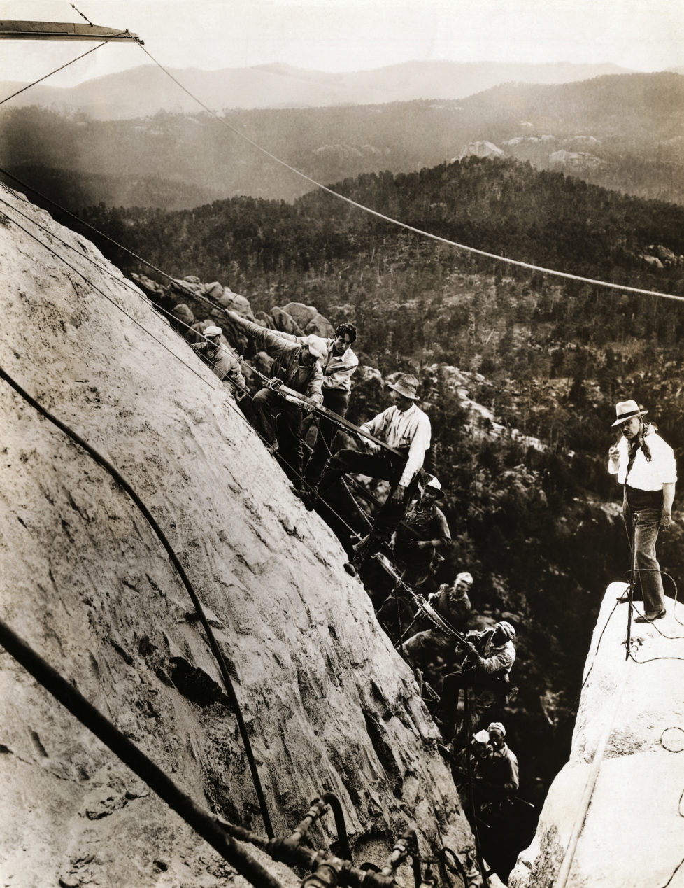 American sculptor Gutzon Borglum (r), who is leading the Mount Rushmore National Memorial project, stands on top of Mount Rushmore with a gang of his sculptors, finishing and smoothing the great granite cliff that will form part of the memorial. The sculptors are standing on the section which will become the forehead of George Washington. (Photo by George Rinhart/Corbis via Getty Images)