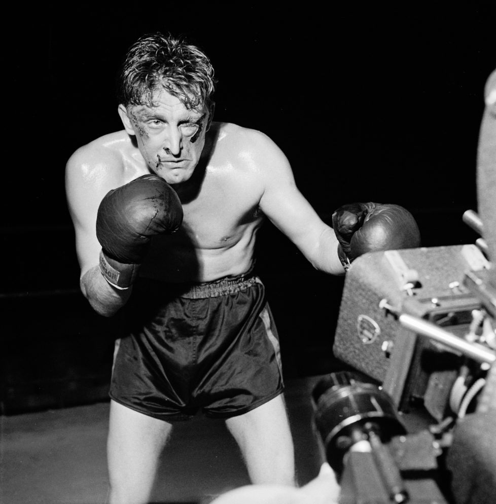 American actor Kirk Douglas poses in front of a movie camera for a publicity still to promote his film 'Champion,' directed by Mark Robson, 1949. Douglas wears boxing gloves and shorts, and sports makeup simulating a swollen left eye and bloody cuts. (Photo by Peter Stackpole/The LIFE Picture Collection/Getty Images)