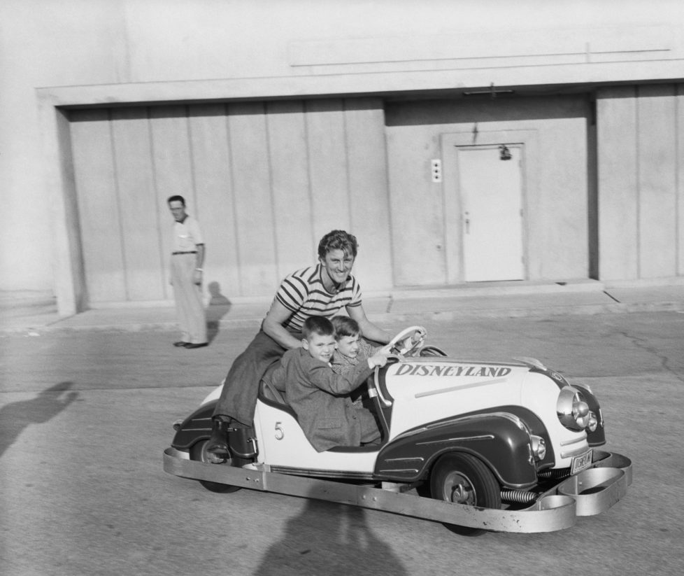 Kirk Douglas shares some automotive thrills with his two sons, Joel (left) and Michael (right), in one of the miniature roadsters at Disneyland. Producer Walt Disney has planned a $9,000,000 project showing the land of the future, and a highlight is to be a miniature freeway in which the youngsters will drive model cars.